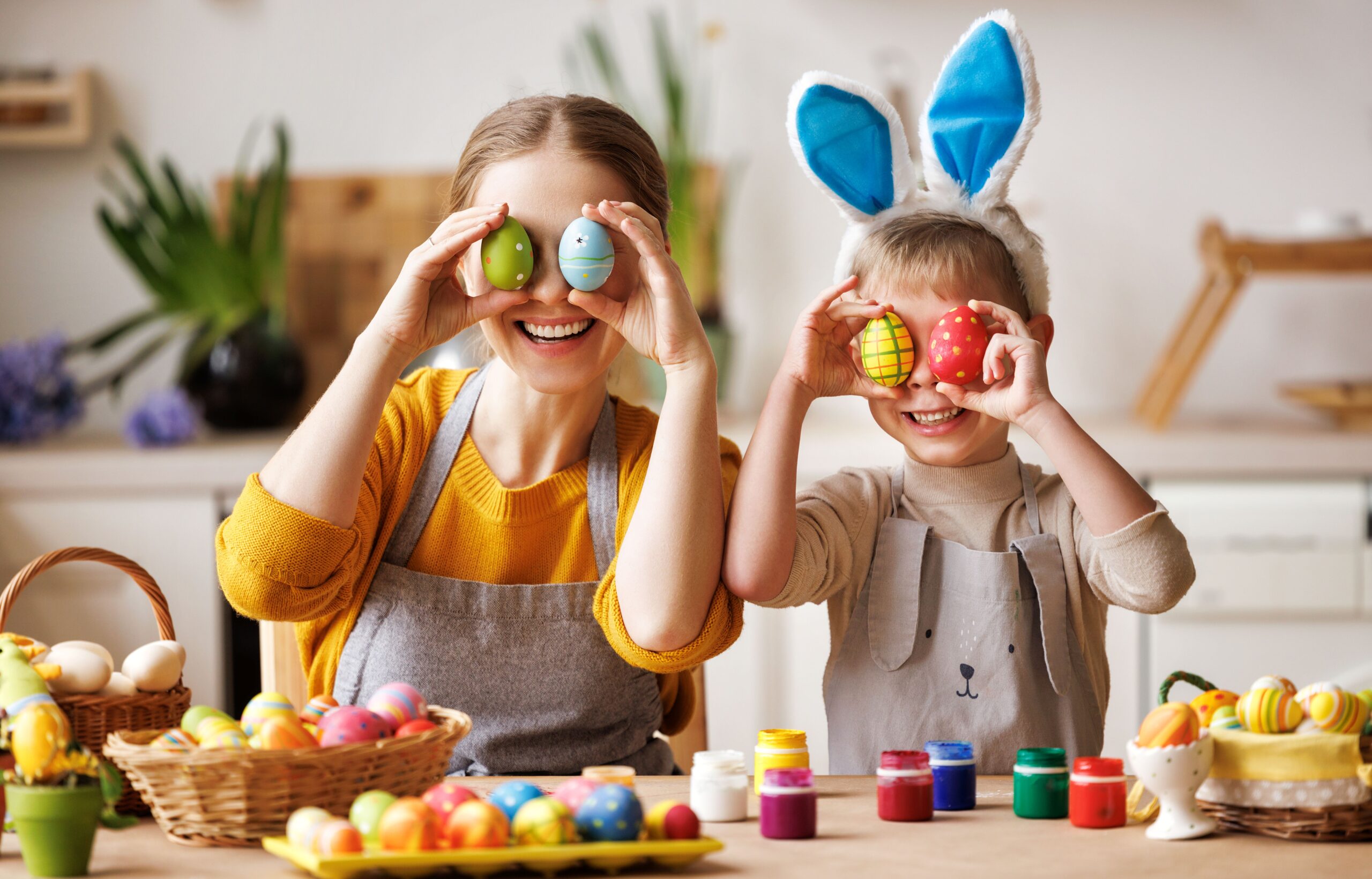 Two children holding up 2 painted eggs in front of their eyes. One of the girls is wearing bunny ears headdress