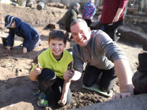 Boy and man showing an archaeological find in a trench