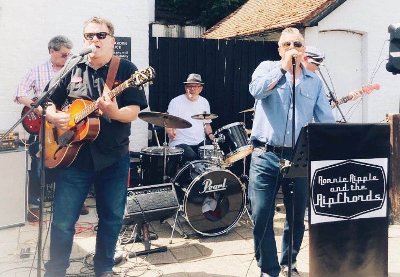 3 male musicians one on guitar, another on drums with a lead singer