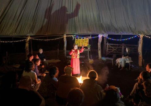 Lady by a fire standing up telling stories