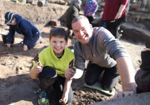 Boy and man showing an archaeological find in a trench
