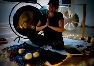 lady sat cross legged in front of a pair of gongs